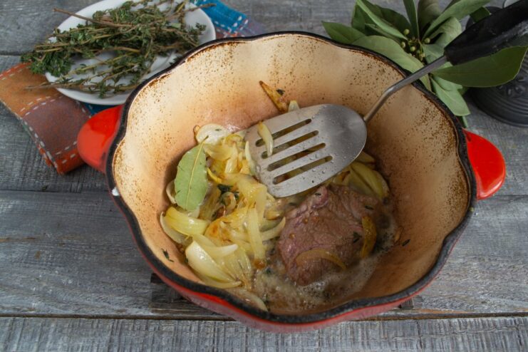 Searing the flour-dredged beef to lock in juices before stewing. Flour-coated beef slices being seared in a pan before being added to the braiser.