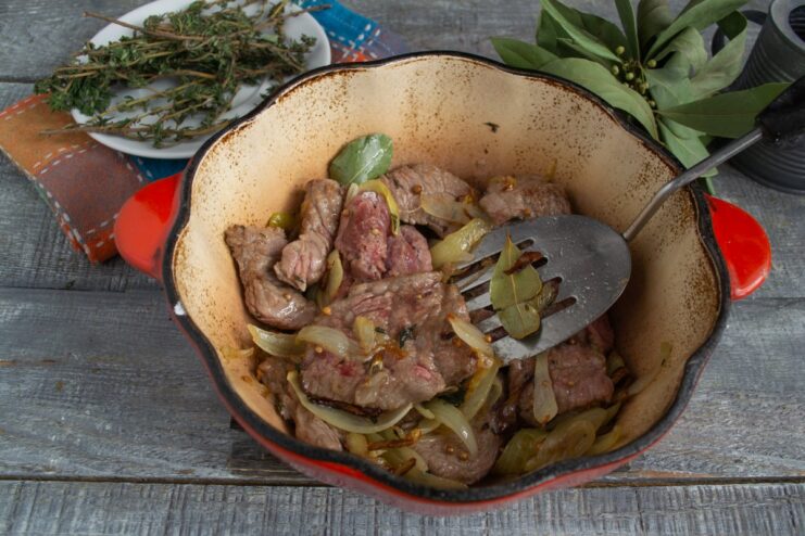 Combining the seared beef with caramelized shallots in the braiser. Seared beef pieces being mixed with sautéed shallots in a large braiser.