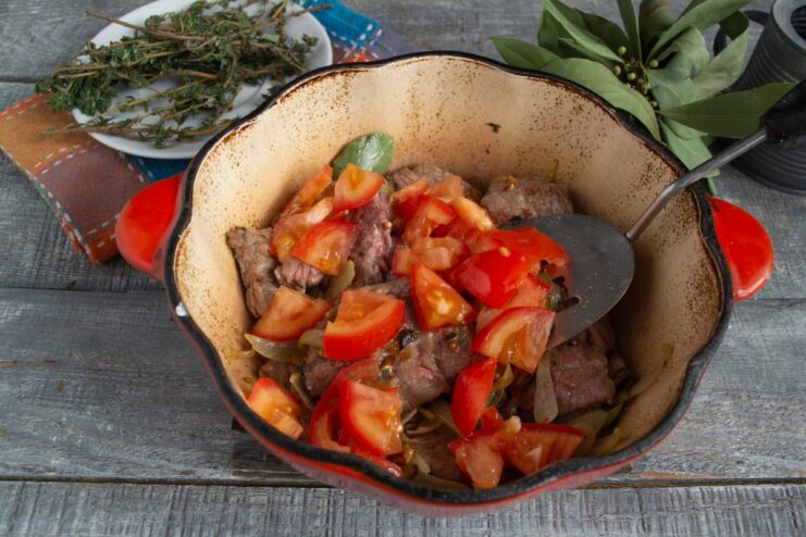 Adding fresh diced tomatoes to the beef and onion mixture. Diced red tomatoes being added to the beef and shallots in the braiser.
