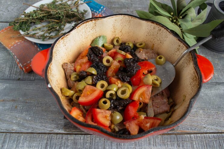 Adding prunes and green olives for a sweet and savory flavor contrast. Sliced prunes and halved green olives being added to the beef stew.