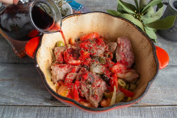 Adding red wine and chicken broth to create the rich braising liquid. Red wine and chicken broth being poured into the braiser over the beef and vegetables.