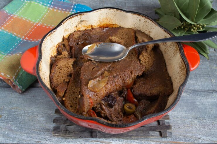 Slow-cooking the beef stew until the meat is tender and the flavors meld. The braiser with the Borodinsky bread topping simmering on a stovetop.