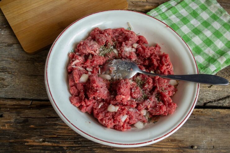 Mixing the Ground Beef with Onion and Spices A bowl of ground beef mixed with finely chopped onions, salt, and pepper.