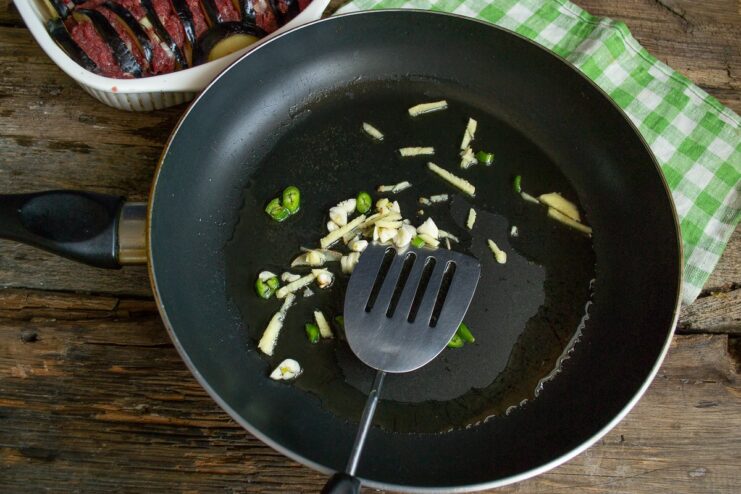 Sautéing Aromatics for the Sauce Chopped ginger, garlic, and chili pepper sizzling in hot olive oil in a frying pan.