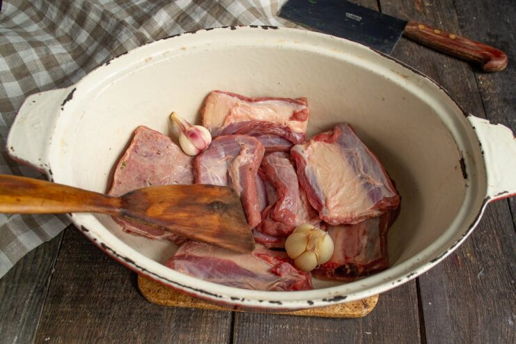 Starting the Beef Rib Stew: Searing Meat with Garlic Raw beef ribs and whole garlic heads in a braiser with oil, ready for cooking.