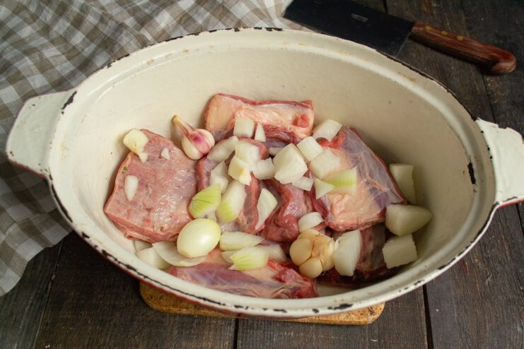 Layering Flavors: Adding Onions to the Beef Ribs Chopped onions being added on top of beef ribs in a braiser.