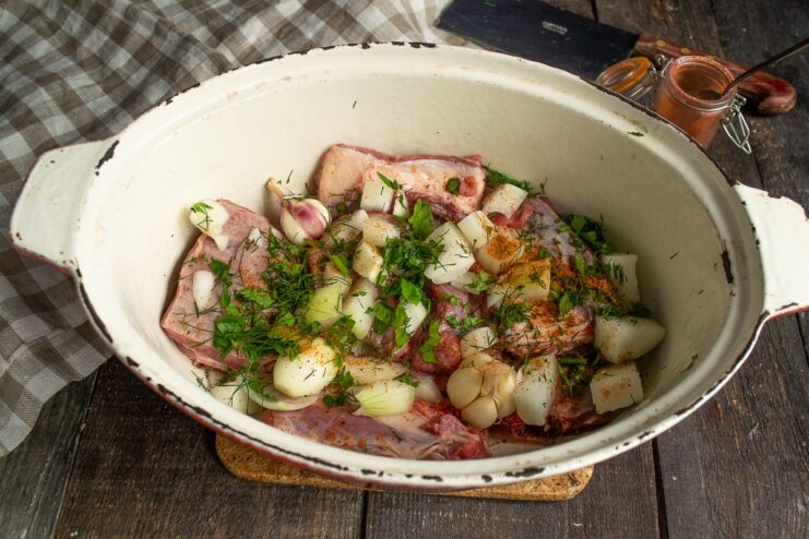 Seasoning the Stew: Adding Herbs and Spices Beef ribs and onions in a pot being seasoned with chopped herbs and a spice mix.