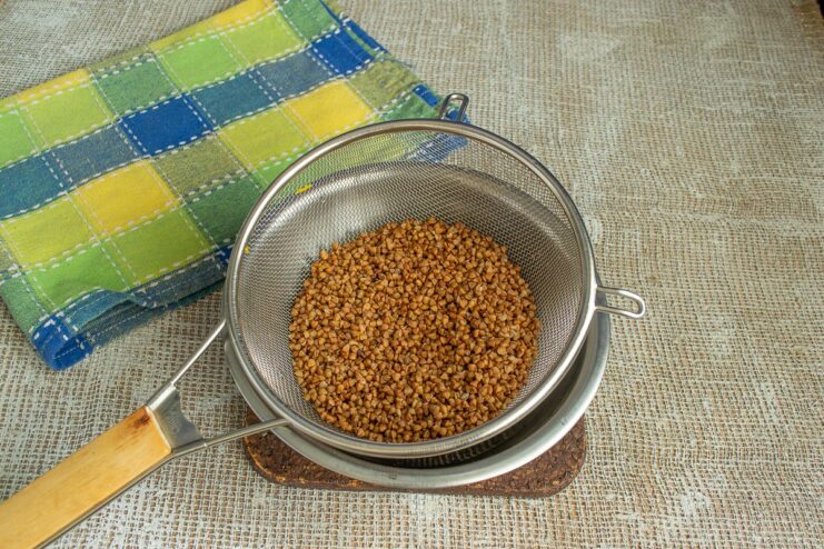 How to Properly Prepare Buckwheat Groats Before Cooking Buckwheat groats in a metal colander being rinsed under running water.