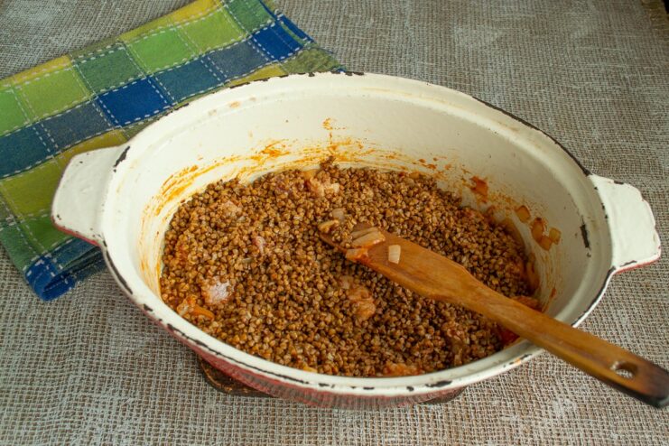 Layering the Ingredients: Adding Buckwheat Over the Pork Rinsed buckwheat groats spread in an even layer over the seared pork in a roasting pan.