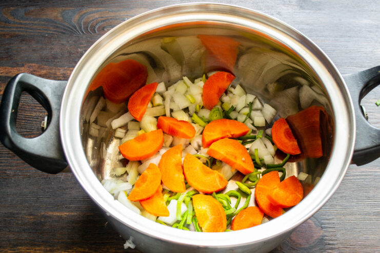Adding Carrots for Sweetness and Color Sliced carrots being added to the pot with onions.
