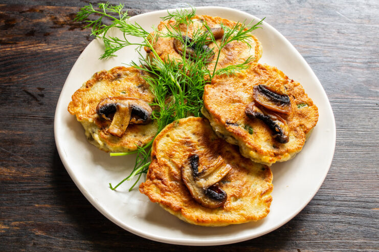 Serving Mushroom Fritters with Smetana or Yogurt Sauce A finished plate of mushroom and garlic scape fritters, garnished with dill and served with a side of smetana.