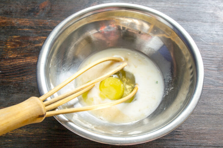 Whisking Eggs and Milk for the Fritter Batter A glass bowl with eggs and milk being whisked together to form the base of the fritter batter.