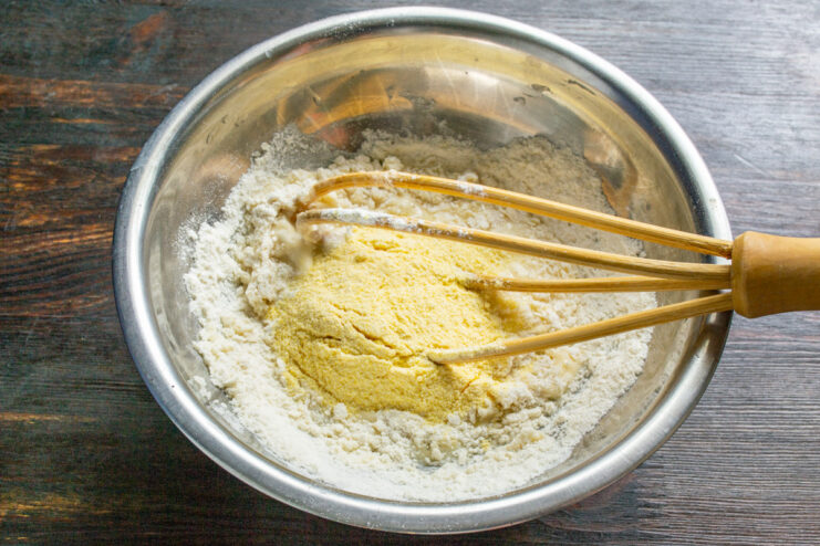 Adding Flour to the Fritter Batter Adding a mix of wheat and corn flour into the egg and milk mixture in a glass bowl.