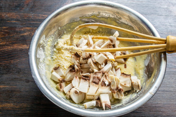 Adding Diced Mushrooms to the Batter Diced fresh champignons being added to the savory fritter batter in a glass bowl.