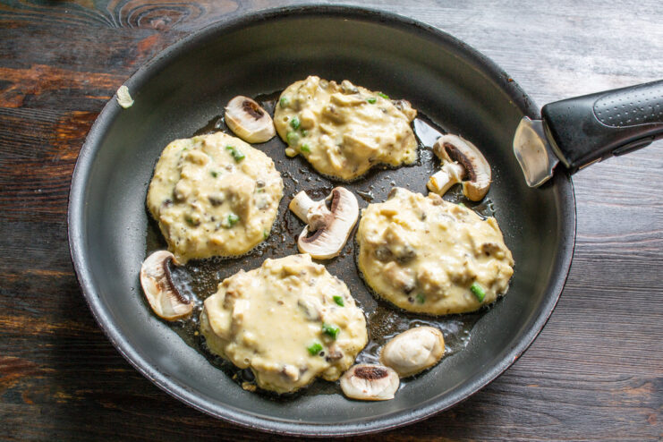 Frying the Mushroom and Garlic Scape Fritters Spoonfuls of mushroom fritter batter being dropped into a hot frying pan with oil.