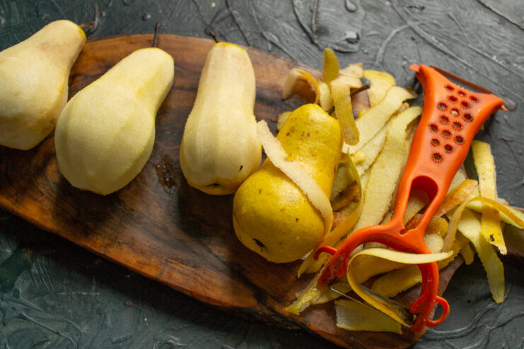 Step 1: How to Prepare Pears for Poaching A person's hands peeling large green pears with a vegetable peeler over a wooden board.