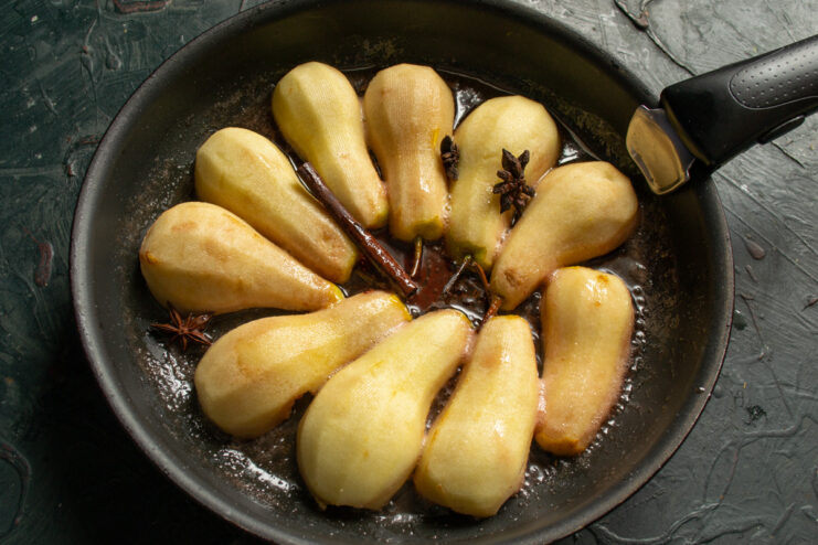 Step 4: Poaching the Pears in Spiced Syrup Pear halves simmering cut-side down in a dark syrup with a cinnamon stick and star anise.