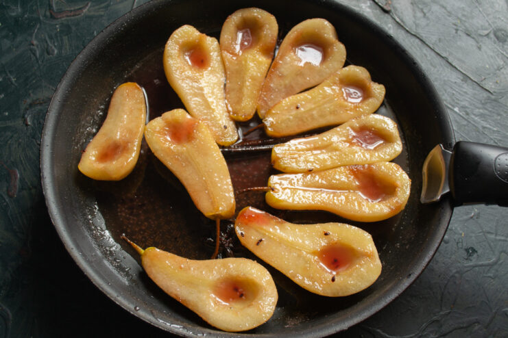 Step 5: Flipping Pears for Even Cooking A hand using kitchen tongs to carefully turn over a poached pear half in a skillet.
