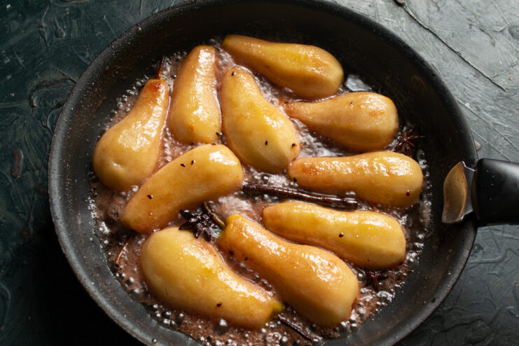 How to Know When Poached Pears Are Done A close-up shot of perfectly poached, translucent pear halves in a bubbling, dark syrup.