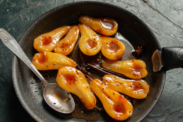 Step 6: Infusing the Pears with Cognac Pouring cognac from a bottle into the skillet containing the poached pears and syrup.
