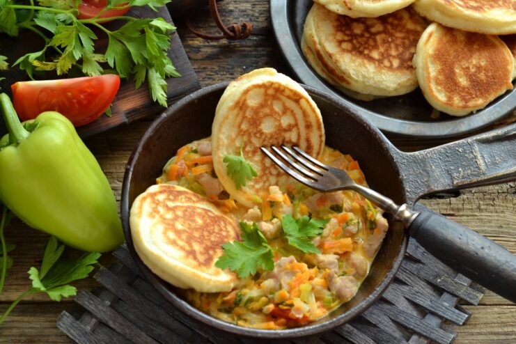 A plate of summer machanka, a pork goulash, served with a stack of fluffy kefir pancakes on the side.