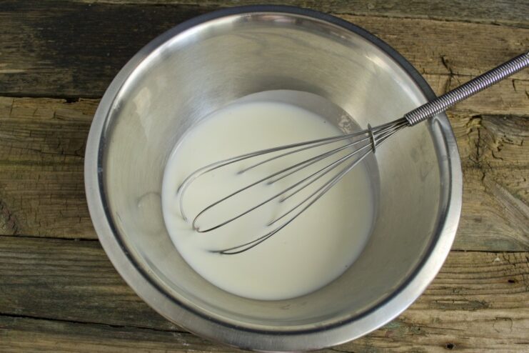 Preparing the Pancake Batter: Mixing Kefir and Seasonings A glass bowl containing kefir being mixed with salt and sugar to start the pancake batter.