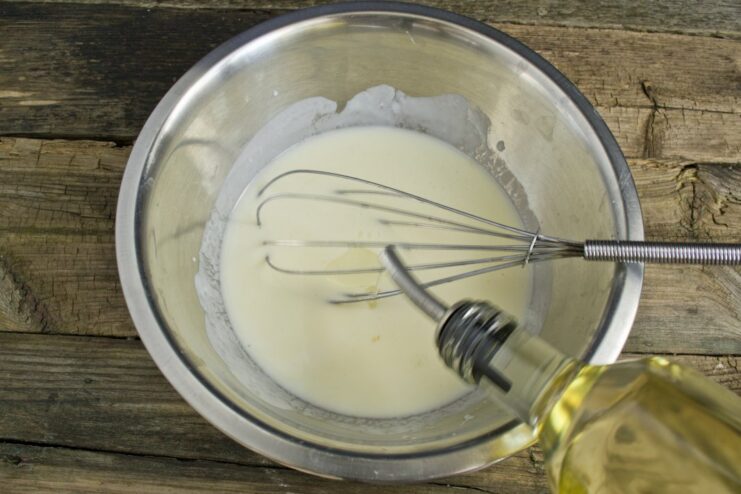Adding Wet Ingredients for Fluffy Pancakes Adding an egg and olive oil to the kefir mixture in a glass bowl for the pancake batter.