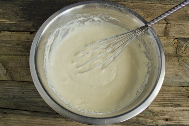 Creating the Perfect Pancake Batter Consistency Adding sifted flour to the wet ingredients in a bowl to create a smooth pancake batter.