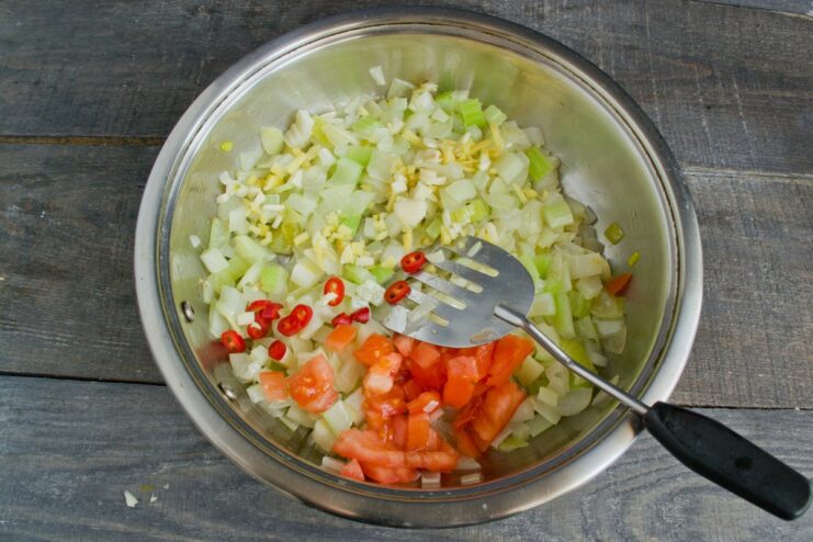 Adding fresh chili, ginger, and tomatoes to create a rich and spicy sauce base Chopped tomatoes, chili, and ginger being added to the vegetables in the pan.