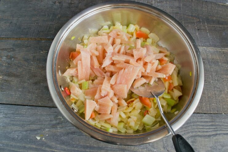 Searing chicken strips with the vegetable mix until lightly browned Strips of chicken breast being fried with a mix of vegetables in a pan.
