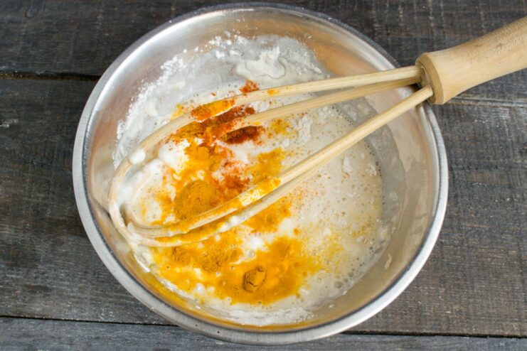 Whisking flour and spices into cream to create a smooth, flavorful sauce A bowl of cream with paprika, turmeric, and flour being whisked together.