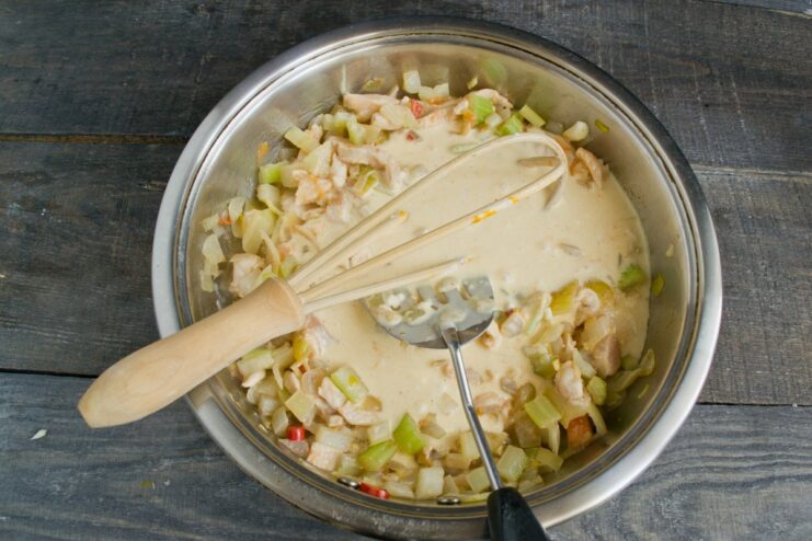Adding the creamy sauce to the chicken and vegetables to create the goulash Pouring the cream and spice mixture into the pan with chicken and vegetables.