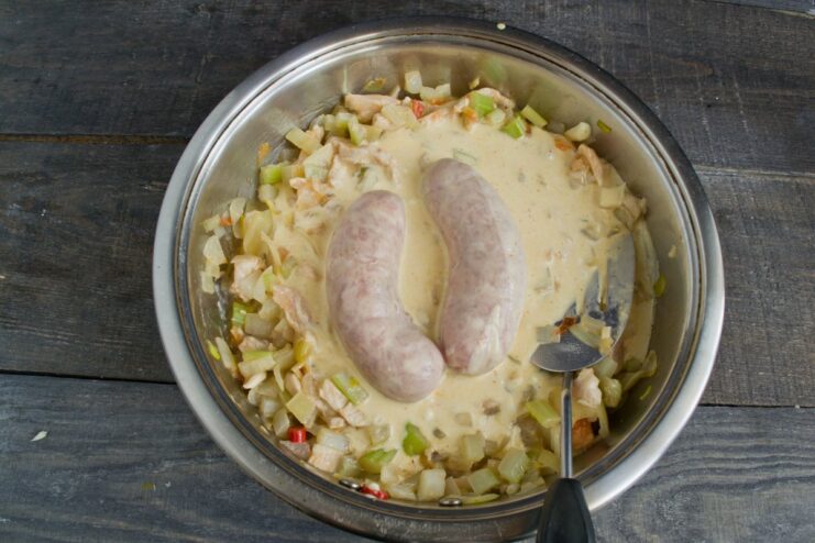 Simmering the raw chicken sausages in the goulash until cooked through Raw chicken sausages simmering in the creamy chicken goulash in a covered pan.