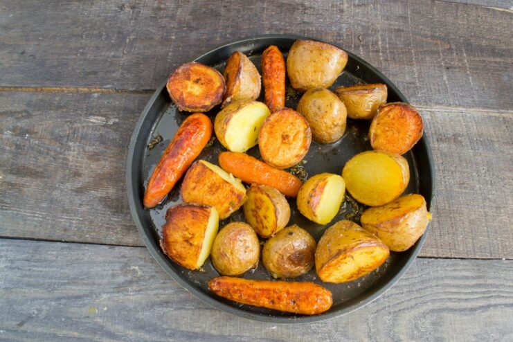 Roasting the vegetables in the oven until they are golden and crispy Potatoes and carrots being roasted in an oven until golden brown.