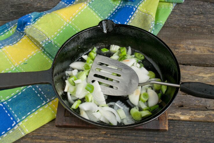 Sautéing Onions to Build a Flavor Base Finely chopped onions being sautéed in a skillet with rendered pork fat.