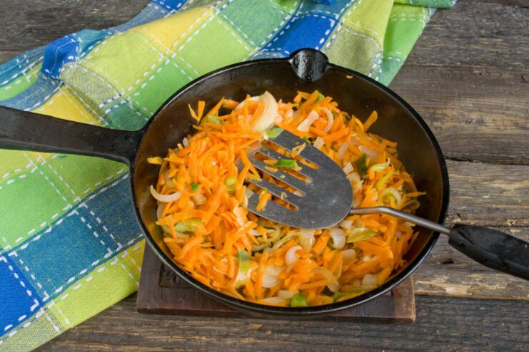 Adding Carrots for Sweetness and Color Grated carrots being sautéed with onions in a skillet.