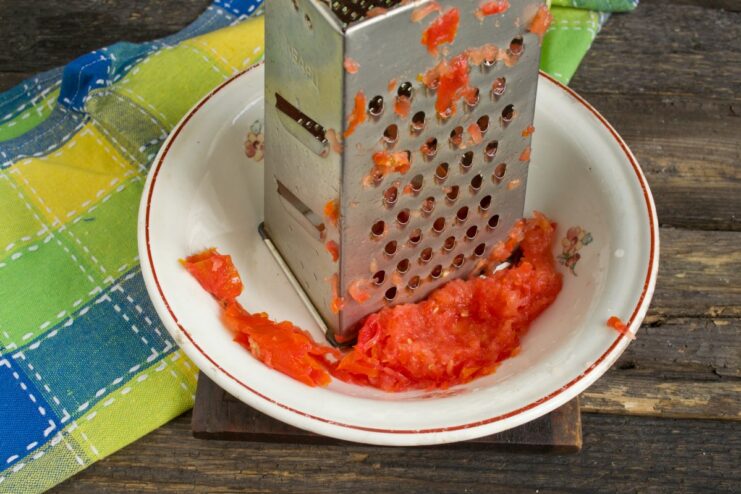 Using Freshly Grated Tomato for a Vibrant Sauce A fresh tomato being grated to create a simple, fresh tomato purée.