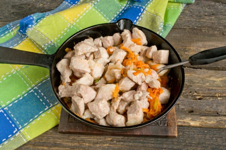 Combining Ingredients for the Goulash Seared pork and fresh tomato purée being added to the sautéed vegetables in the skillet.