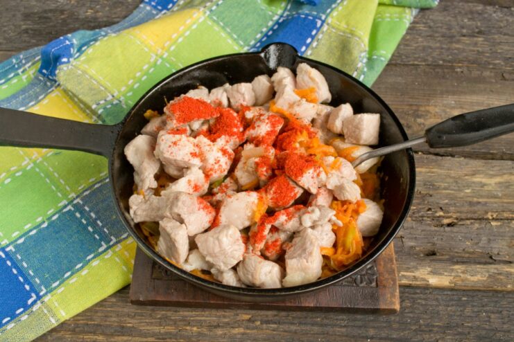 Seasoning the Goulash for a Balanced Flavor Spices, including sweet paprika, salt, and pepper, being added to the pork and vegetables in the skillet.