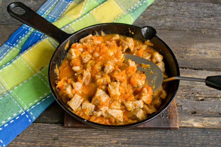 Simmering the Goulash to Tenderness Pork goulash simmering in a skillet, with liquid being added to create a gravy.