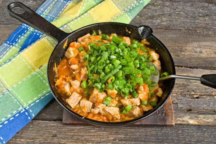 Finishing with Fresh Green Onions Finely chopped green onions being added to the cooked pork goulash in the skillet.