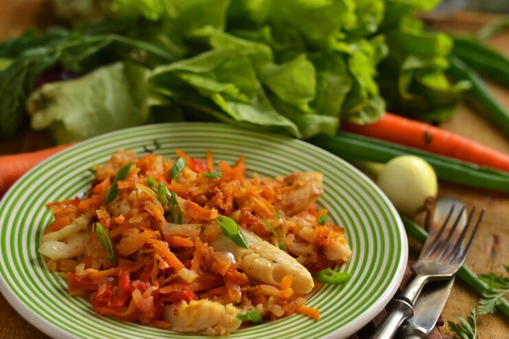 A plate of cooked hake with stewed vegetables, garnished with fresh herbs.