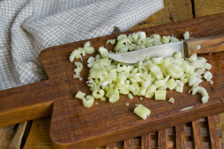 Adding Celery to the Sautéed Onions Finely chopped celery being added to the skillet with sautéed onions.