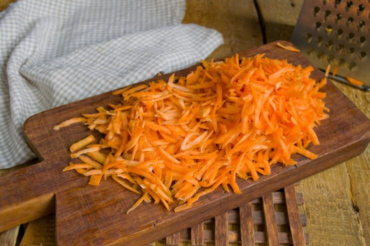 Stewing Carrots with Other Vegetables Shredded carrots being added to the skillet with onions and celery to stew.