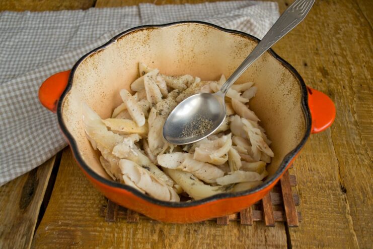 Placing Flaked Hake in a Dutch Oven Pieces of cooked, flaked hake being placed at the bottom of a Dutch oven.