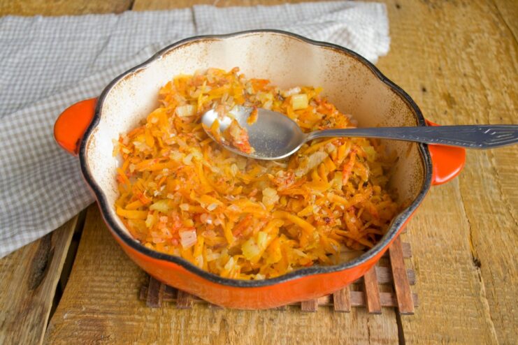 Layering Stewed Vegetables Over the Hake A layer of stewed vegetables being spread over the flaked hake in a pot.