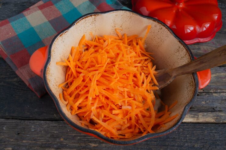 Adding grated carrot to the onions for the sauce Grated carrot being added to the skillet with sautéing onions.