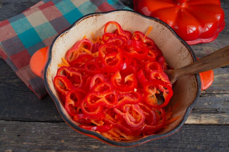 Adding sliced bell pepper to the vegetable mix Sliced red bell pepper being added to the skillet with onions and carrots.