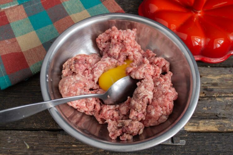 Adding an egg to the ground meat for the meatballs An egg being cracked into a bowl of ground meat.