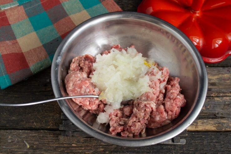 Mixing grated onion into the ground meat Grated onion being added to the bowl with ground meat and egg.